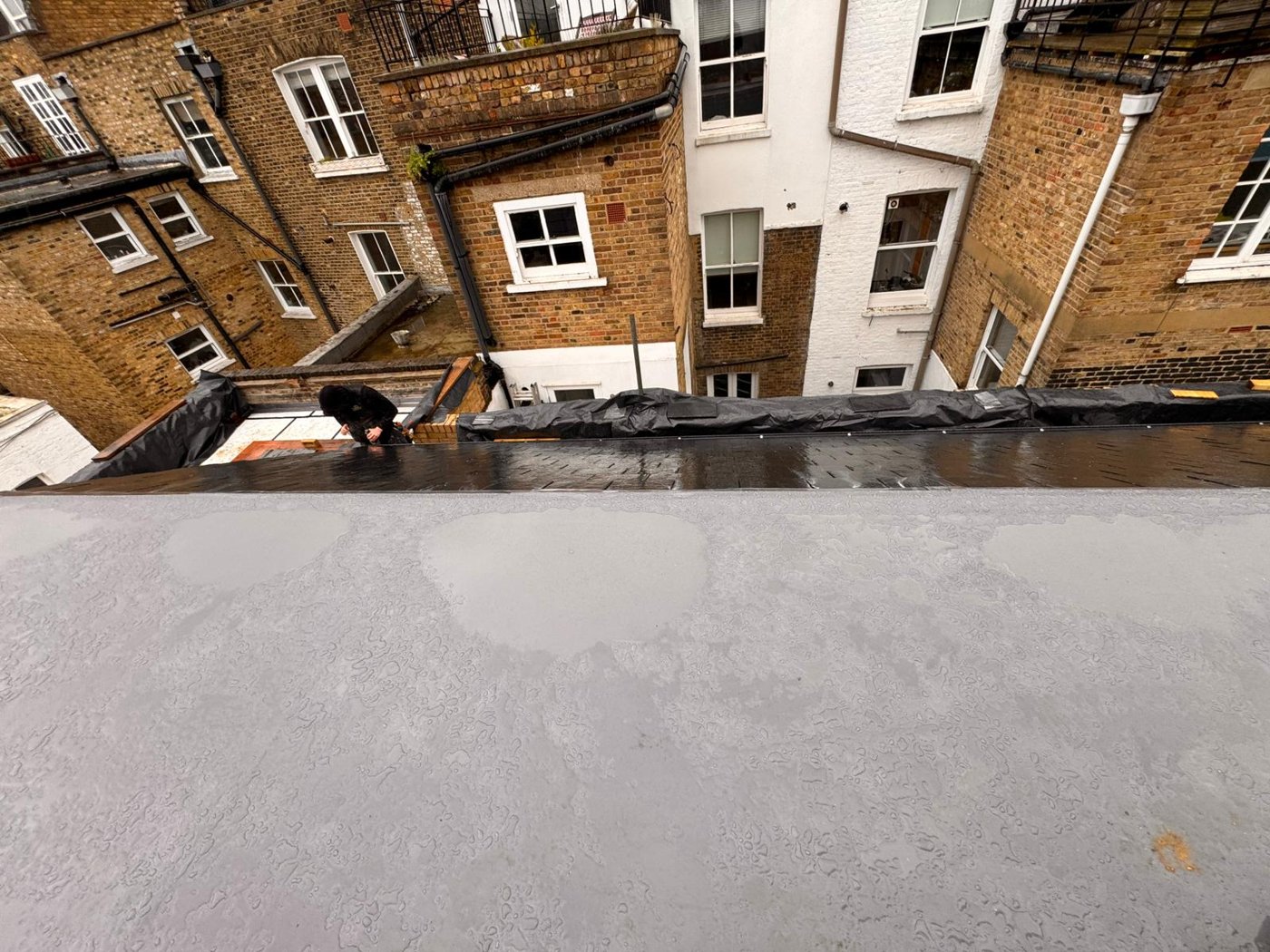Flat roof covering installation in progress with a worker in the background